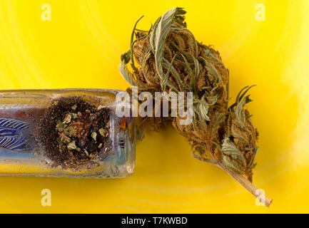 Overhead Ansicht schließen einer Marihuana bud auf gelbem Hintergrund mit einem kleinen Generic pipe mit natürlichem Licht beleuchtet. Stockfoto