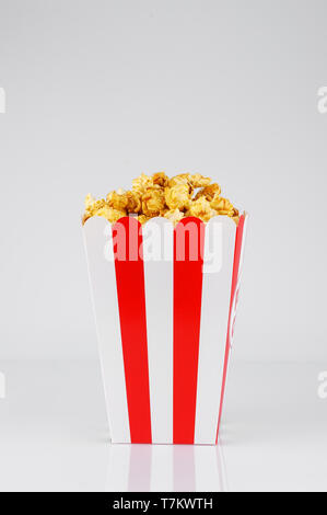 Karamell Popcorn in gestreiften Papier roten und weißen line Box auf weißem Hintergrund. Snacks und Essen für einen Film. Vertikale Ausrichtung. Stockfoto