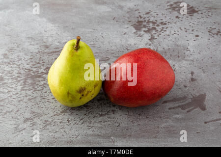 Seitliche Sicht auf zwei grüne und rote reife Anjou Birnen auf einem grauen gesprenkelter Hintergrund mit natürlichem Licht beleuchtet. Stockfoto