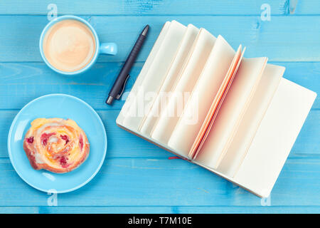 Tasse Kaffee mit Kuchen und ein offenes Buch auf einem blauen Hintergrund aus Holz Stockfoto