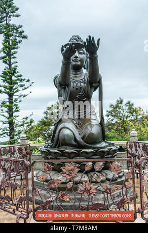 Hong Kong, China - 7. März 2019: Insel Lantau. Eine der sechs Devas bietet Obst zum Tian Tan Buddha. Bronzestatue von vorne gesehen mit grünen foliag Stockfoto