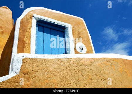 Gelbes Gebäude mit blauen Tür gegen einen blauen Himmel mit Wolken in Oia, Santorini, Griechenland Stockfoto