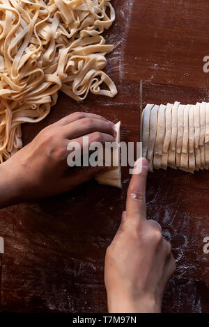 Junge Haus Frau Vorbereiten der hausgemachte Pasta in der Küche. Frau lange Streifen schneiden Teig für das Kochen von Nudeln. Hausgemachte Speisen Vorbereitung Konzept. Stockfoto