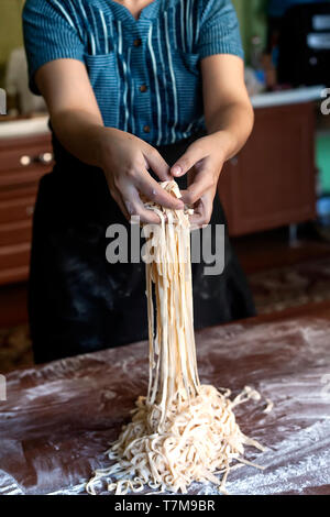 Junge Haus Frau Vorbereiten der hausgemachte Pasta in der Küche. Frau lange Streifen schneiden Teig für das Kochen von Nudeln. Hausgemachte Speisen Vorbereitung Konzept. Stockfoto