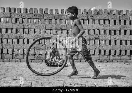 Kolkata: vom 04.02.2018, einem Dorf in der Nähe von Backstein kilin leben die Menschen in den Schlamm Häuser, Kinder spielen mit Abfällen Reifen tragen Füße laufen zu lassen, kleine Mädchen si Stockfoto
