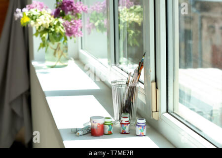 Glas mit Pinsel und Farben auf der Fensterbank Stockfoto