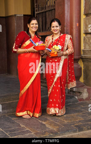 Frauen in bunten Saris in Rot und Gold halten religiöse Angebote in Pashupatinath Hindu Tempel, Tal von Kathmandu, Nepal Stockfoto