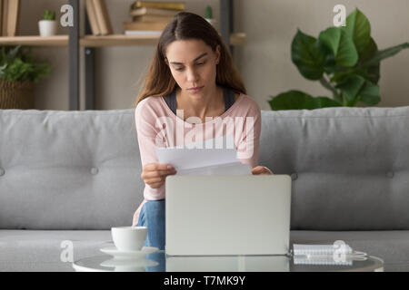 Ernsthafte Frau sitzt auf der Couch Lesen Schreiben ist frustriert, Stockfoto