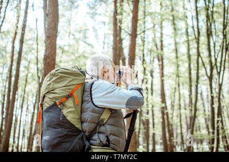 Ältere Menschen, die mit dem Fernglas unterwegs mit Rucksack in den Wald Stockfoto