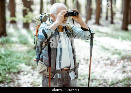 Ältere Menschen, die mit dem Fernglas unterwegs mit Rucksack in den Wald Stockfoto