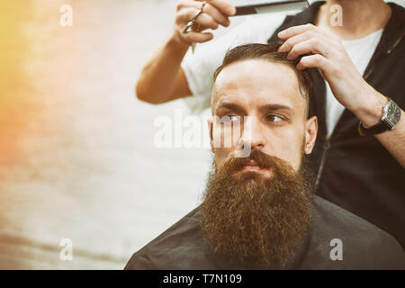 Meister schneidet Haare und Bart von Männern im Frisörsalon, macht Friseur Frisur für einen jungen Mann Stockfoto