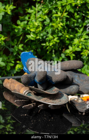 Garten Werkzeuge einschließlich Gabel, Kelle, Rosenscheren und Handschuhe auf ein Glas Terrasse Tisch mit einer Anlage im Hintergrund reflektiert Stockfoto