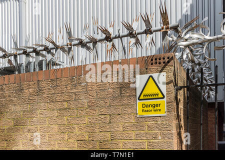 Stacheldraht auf eine Mauer mit einem Warnschild unterhalb, Großbritannien Stockfoto