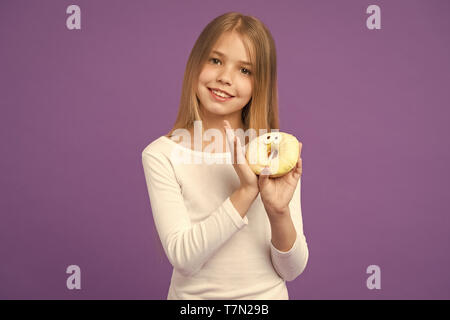 Möchten Sie ein glückliches Kind mit Junk Food. Kind Lächeln mit Donut auf Violett Hintergrund. Kleines Mädchen mit glasierten ring Donut auf lila Hintergrund. Essen und Nachtisch. Kindheit und Kinderbetreuung. Stockfoto