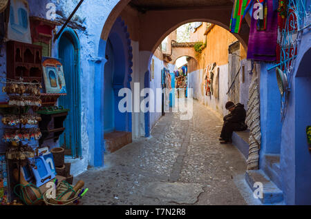 Chefchaouen, Marokko: ein Mann sitzt unter einem Bogen im blau getünchten Gassen der Medina, der Altstadt. Stockfoto