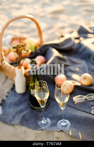 Fokus auf Flasche Champagner und Gläsern, Korb mit Früchten auf Plaid und Sand Strand in verschwommenen Hintergrund. Konzept der Picknick Komposition. Stockfoto
