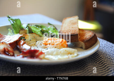 Englisches Frühstück Spiegelei mit Speck Wurst, Brot und Salat Stockfoto