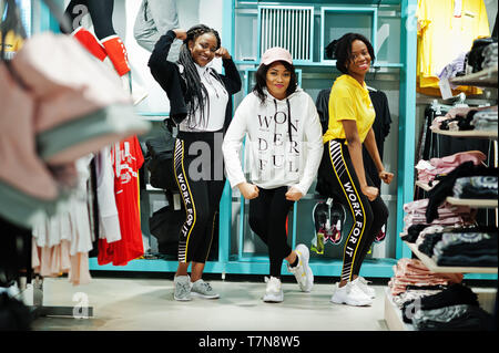 Drei afican amerikanische Frauen in Trainingsanzügen einkaufen bei Sportswear Mall gegen Regale. Sport store Thema. Stockfoto