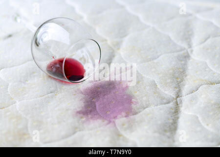 Wein Glas verschüttet auf dem Bett. Fallengelassen Weinglas auf weißen Bettlaken. Rosa nassen Fleck. Pech, unglückliche Situation. Stockfoto
