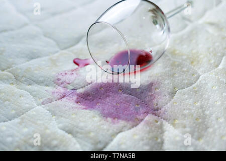 Wein Glas verschüttet auf dem Bett. Fallengelassen Weinglas auf weißen Bettlaken. Rosa nassen Fleck. Pech, unglückliche Situation. Stockfoto