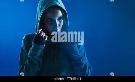 Fitness-Frau mit Kapuzenhemd und Straps an den Händen. Frau, die auf den Kopierraum vor blauem Hintergrund blickt. Stockfoto