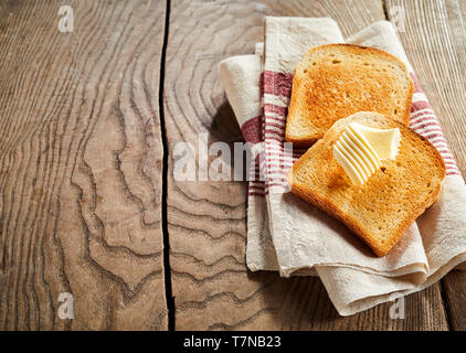 Zwei Scheiben golden knuspriges Weißbrot, Toast mit einem dekorativen Spule von Butter auf einer Serviette auf einem rustikalen Holztisch mit Kopie Raum Stockfoto