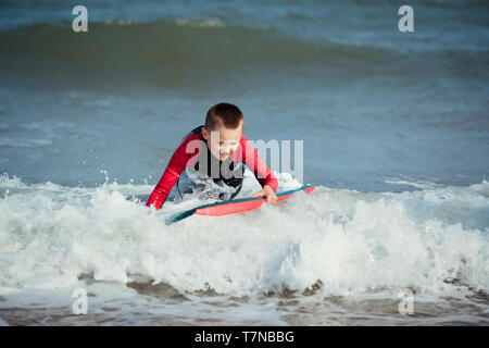 Kleiner Junge versucht, auf seinem Surfbrett im Meer zu stehen. Stockfoto