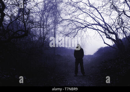 Ein furchtsames Hooded stehenden Figur in einer nebligen Wald im Winter, mit einem harten Blau bearbeiten. Stockfoto