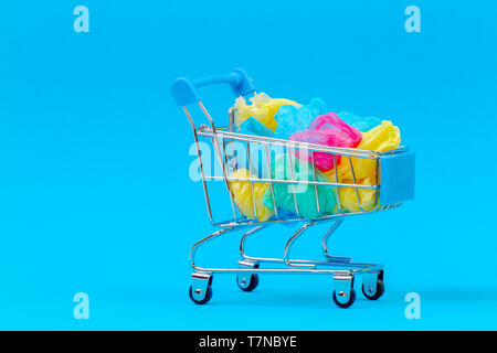 Mini Einkaufswagen voller bunter single use Plastiktüten auf blauem Hintergrund Stockfoto