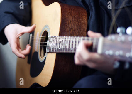Ein Mann in der dunklen Kleidung spielen akustische Holz- 6-saitige Gitarre schöne Melodien und Songs Stockfoto