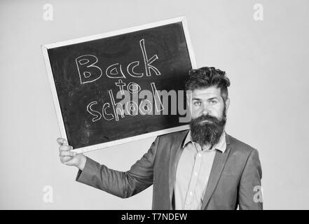 Einladung zum Tag des Wissens zu feiern. Lehrer wirbt Zurück zu studieren beginnen. Lehrer bärtiger Mann steht und hält Tafel mit Inschrift zurück zu Schule grauen Hintergrund. Stockfoto