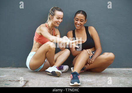 Passen junge Frau in Sportkleidung auf dem Bürgersteig vor Ihrem Workout Partner ihr Sport Übersicht ansehen, während Sie für einen Durchlauf zusammen Stockfoto