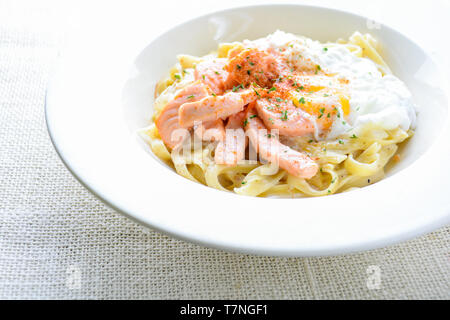 Fettucine mit Lachs, Ei und Parmesan, auf weiße Platte serviert. Stockfoto