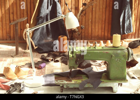 Alte Nähmaschine mit Leder und kunstgewerbliche Gegenstände auf dem Boden in der Werkstatt Stockfoto