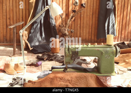 Alte Nähmaschine mit Leder und kunstgewerbliche Gegenstände auf dem Boden in der Werkstatt Stockfoto