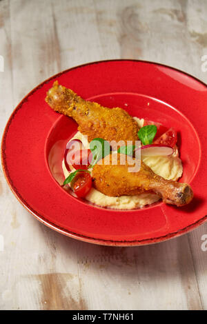 Hähnchenschenkel in loser Schüttung mit Kartoffelpüree und Gemüse auf einem roten Schild. Hellen Hintergrund. Restaurant Menü Stockfoto