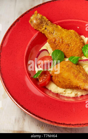 Hähnchenschenkel in loser Schüttung mit Kartoffelpüree und Gemüse auf einem roten Schild. Hellen Hintergrund. Restaurant Menü Stockfoto