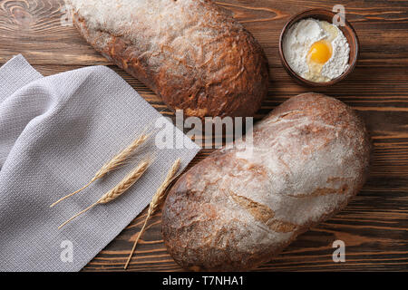 Frische leckere Brot und Schüssel mit weißem Mehl auf Holz- Hintergrund Stockfoto