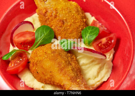 Hähnchenschenkel in loser Schüttung mit Kartoffelpüree und Gemüse auf einem roten Schild. Hellen Hintergrund. Restaurant Menü Stockfoto