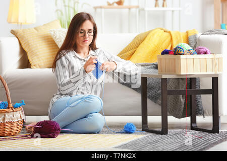 Junge Frau sitzt auf dem Teppich und Stricken warme Pullover zu Hause Stockfoto