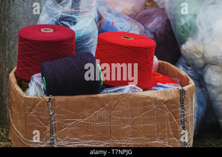 Ein Bündel grosse bunte Thema Spulen in alten Karton auf dem Boden im freien, transparenten Taschen mit nähen Materialien auf Hintergrund Stockfoto