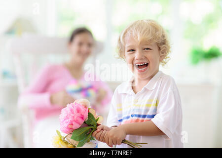 Happy Mother's Day. Kind mit Gegenwart und Blumen für Mama. Little boy Holding verpackte Geschenk und Blumenstrauß für die Mutter. Familie feiern Feder h Stockfoto