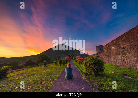 Api-Vulkan bei Sonnenuntergang, sitzt Frau auf der Suche nach Ansicht von Banda Naira fort, Molukken Molukken, Indonesien, Top Travel Tourist Destination, dramatische Himmel. Stockfoto