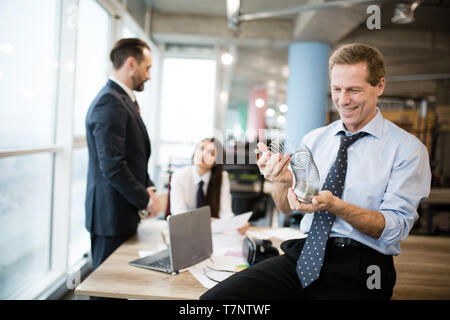 Kaufmann ist Spielen mit einem Blechspielzeug Slinky. Er lächelt mit weißen Helle Zähne beim Sitzen auf der Deskand ein weißes Hemd, Krawatte und Stockfoto