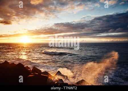 Einen malerischen Sonnenuntergang mit Wellen, die auf Felsen, Puerto de la Cruz, Teneriffa, Spanien. Stockfoto