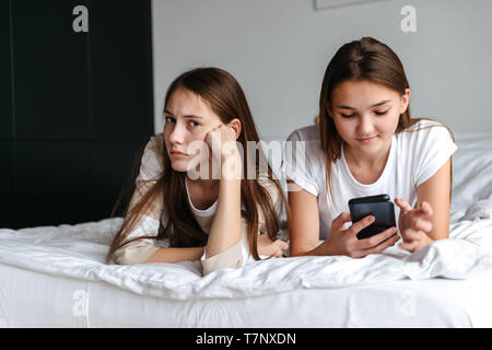 Zwei süße teengae Mädchen Festlegung auf dem Bett, holding Mobiltelefone zu Hause Stockfoto