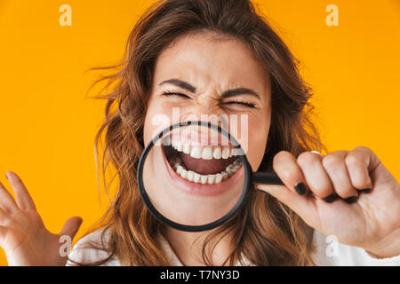 Portrait von eine fröhliche junge Frau tragen weiße Hemd, die auf gelben Hintergrund isoliert, spielen mit Lupe Stockfoto