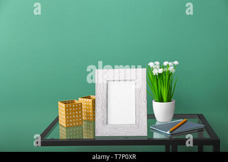 Zusammensetzung mit Bilderrahmen auf Glas Tisch gegen Farbe Hintergrund Stockfoto