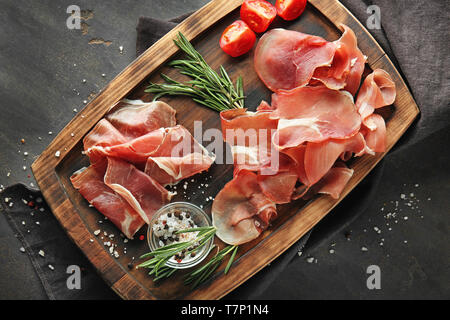 Holzplatte mit leckeren Schinken Scheiben, Tomaten und Kräutern auf Tabelle Stockfoto