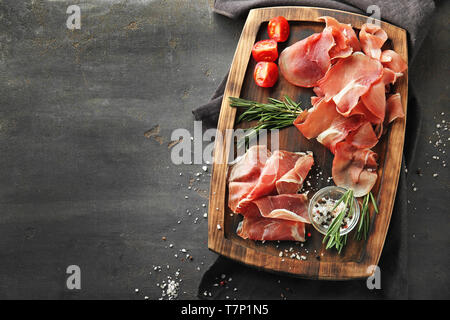 Holzplatte mit leckeren Schinken Scheiben, Tomaten und Kräutern auf Tabelle Stockfoto